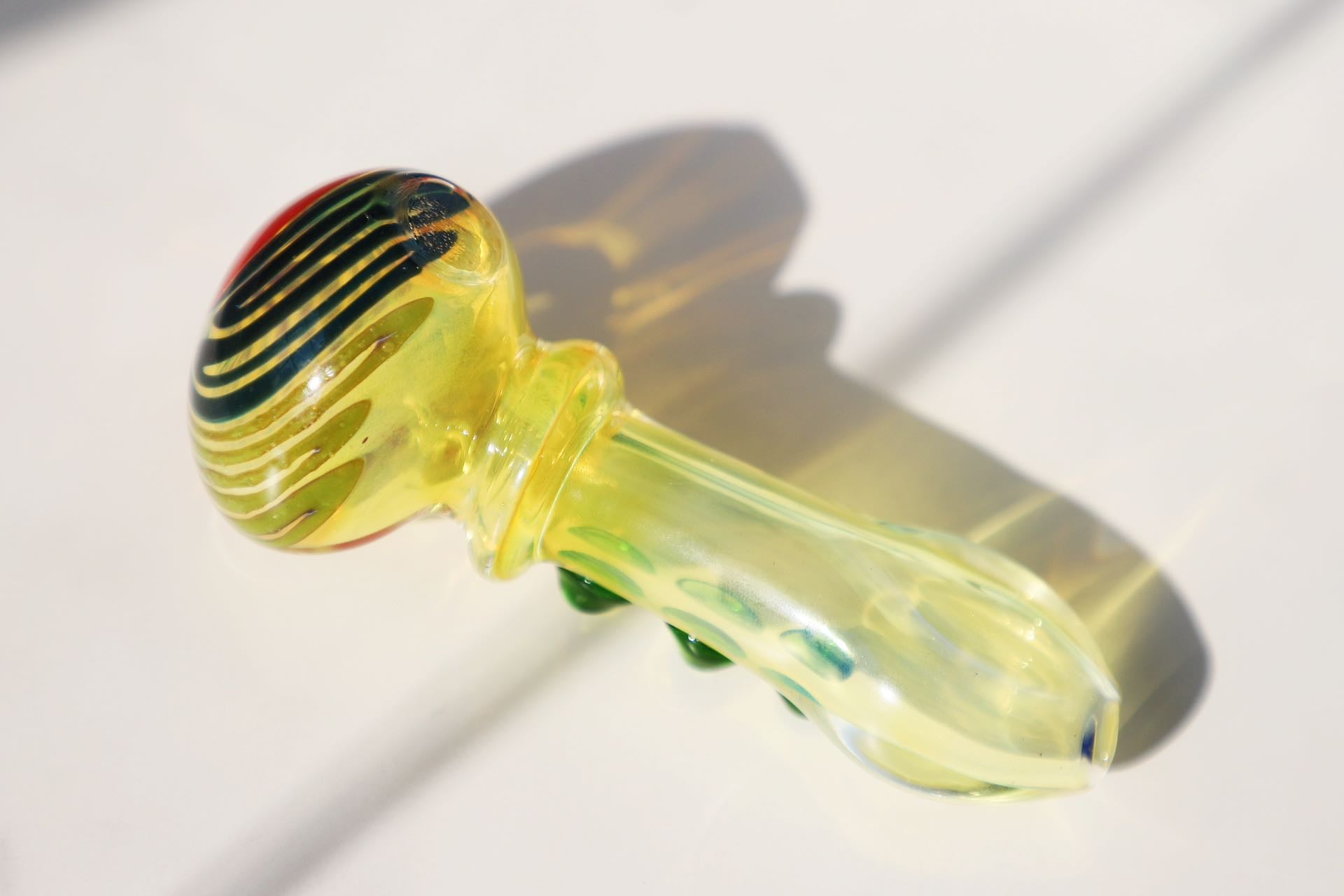 mmerse yourself in the radiance of our Handcrafted Sunburst Yellow Glass Smoking Pipe, featuring vibrant green bubble accents for a tactile experience. This artisanal handblown piece stands out with its unique spiral design, providing both aesthetic pleasure and functional smoking elegance. A perfect match for connoisseurs looking for a pipe that marries artistic craftsmanship with a splash of color for a joyful smoking session.